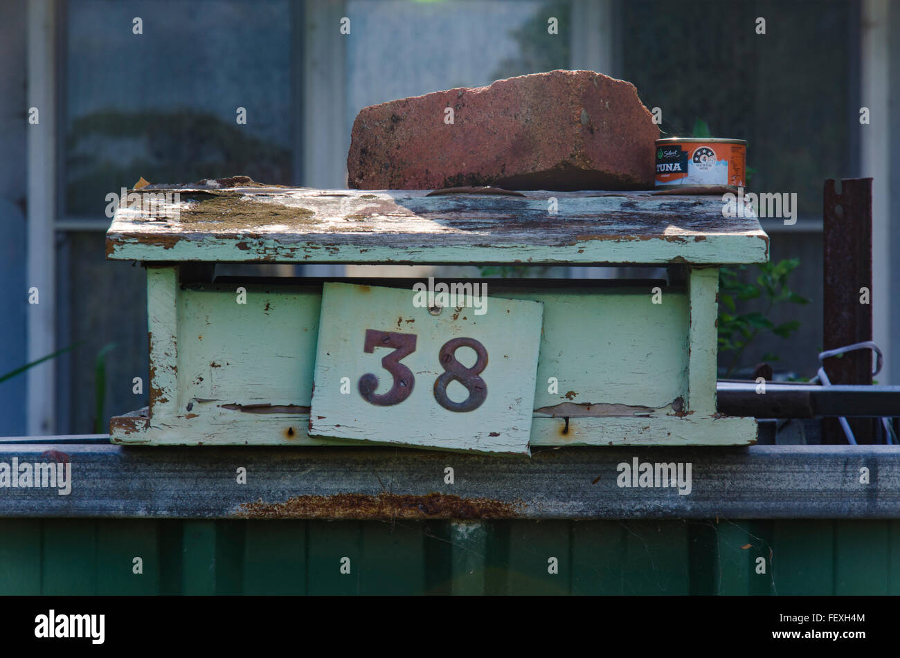 An old timber letterbox sits on a fence held down by a  house brick, number 38 with peeling paint in Australia Stock Photo