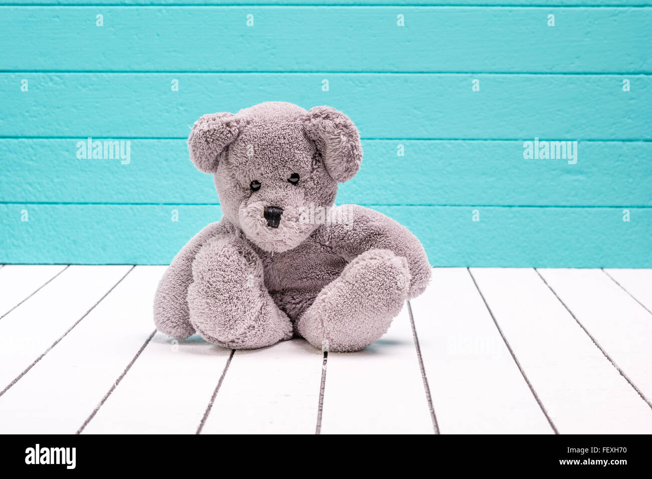 Teddy bear sitting on white wooden floor with bluegreen background
