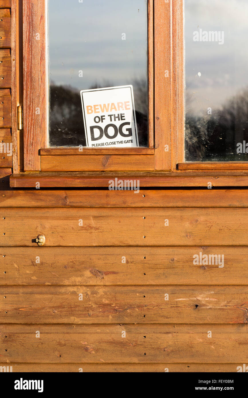 Beware of the dog please close the gate sign in window on brown shed Stock Photo