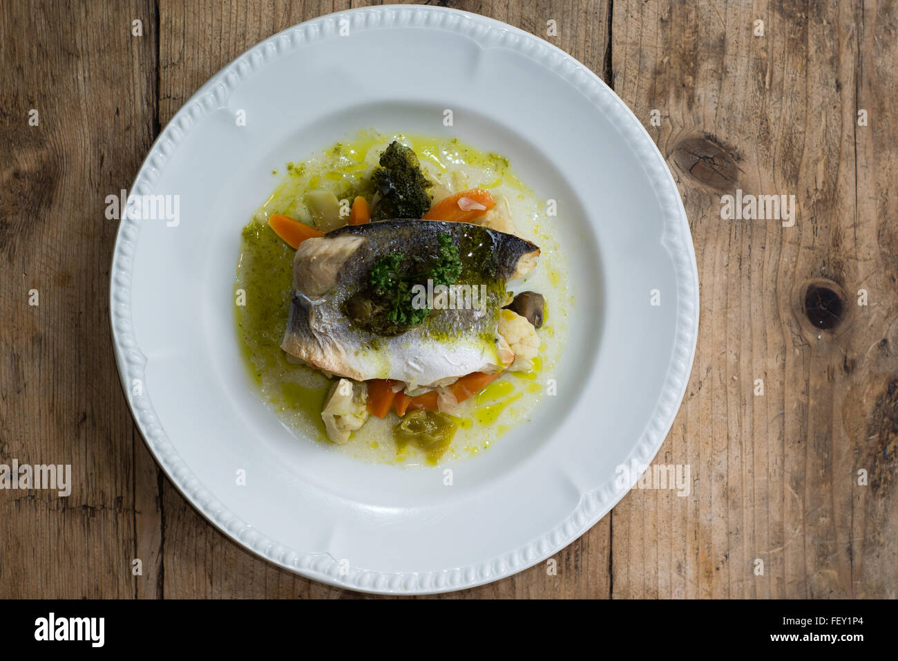 Sea bass with mixed seasonal vegetables on plate. Seabass fillet, mixed seasonal vegetables, lemon-herbs-caper butter Stock Photo