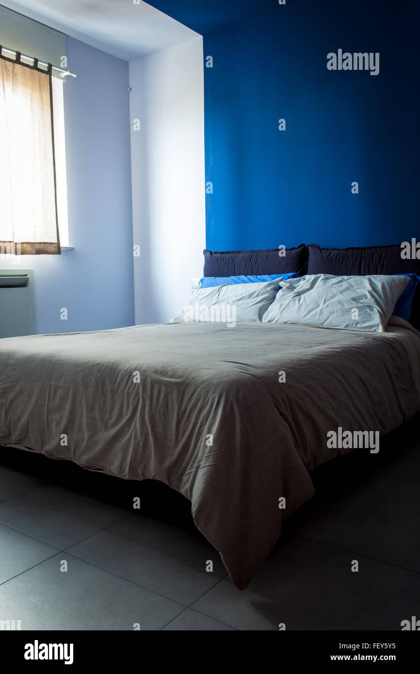 Clean and tidy bedroom, light bedsheets, the main color is blue. Stock Photo