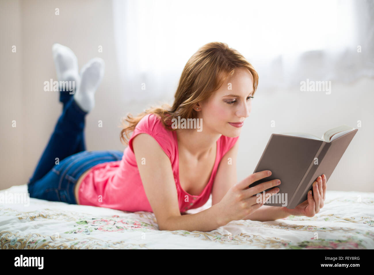 Relaxing woman reading book with a smile in white interior Stock Photo