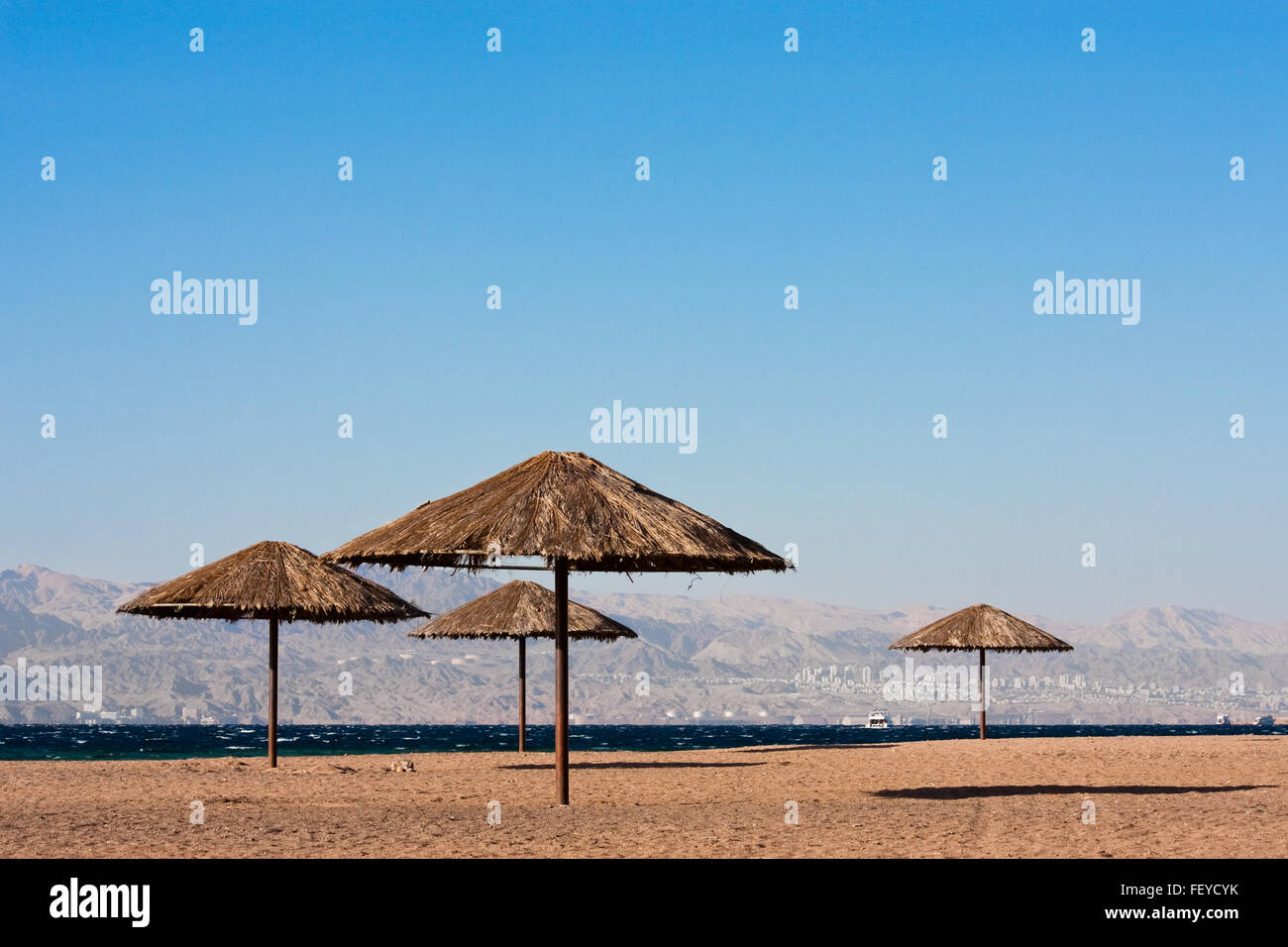 Sunshades near on beach of the Read Sea in Aqaba, Jordan. City of Eilat, Egypt in background. Stock Photo