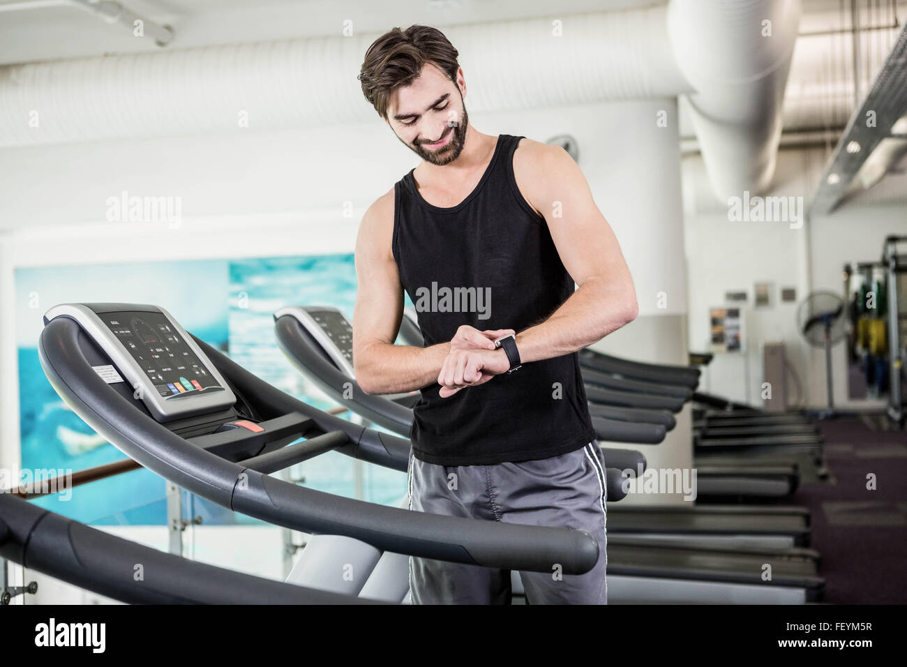 Smiling man on treadmill looking at smartwatch Stock Photo - Alamy