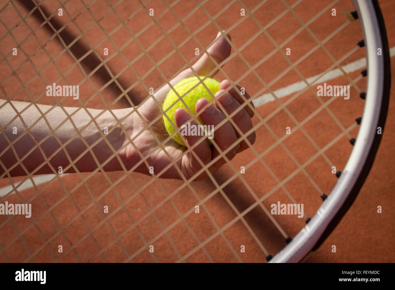 Sportsman's hand holding a tennis ball seen through a racket's string