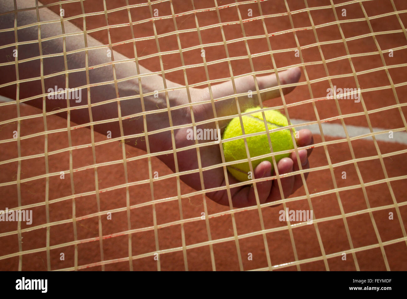 Landscape image of a player's hand holding a tennis ball seen through a racket's string Stock Photo