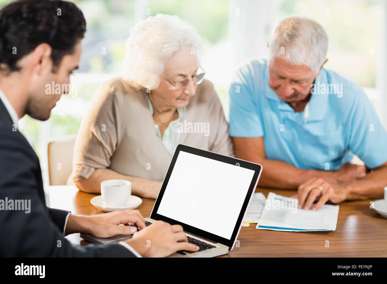 Businessman using laptop while senior couple is reading documents Stock Photo