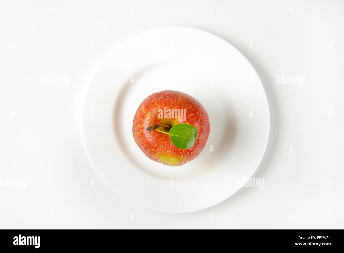 washed red apple with leaf on white plate Stock Photo