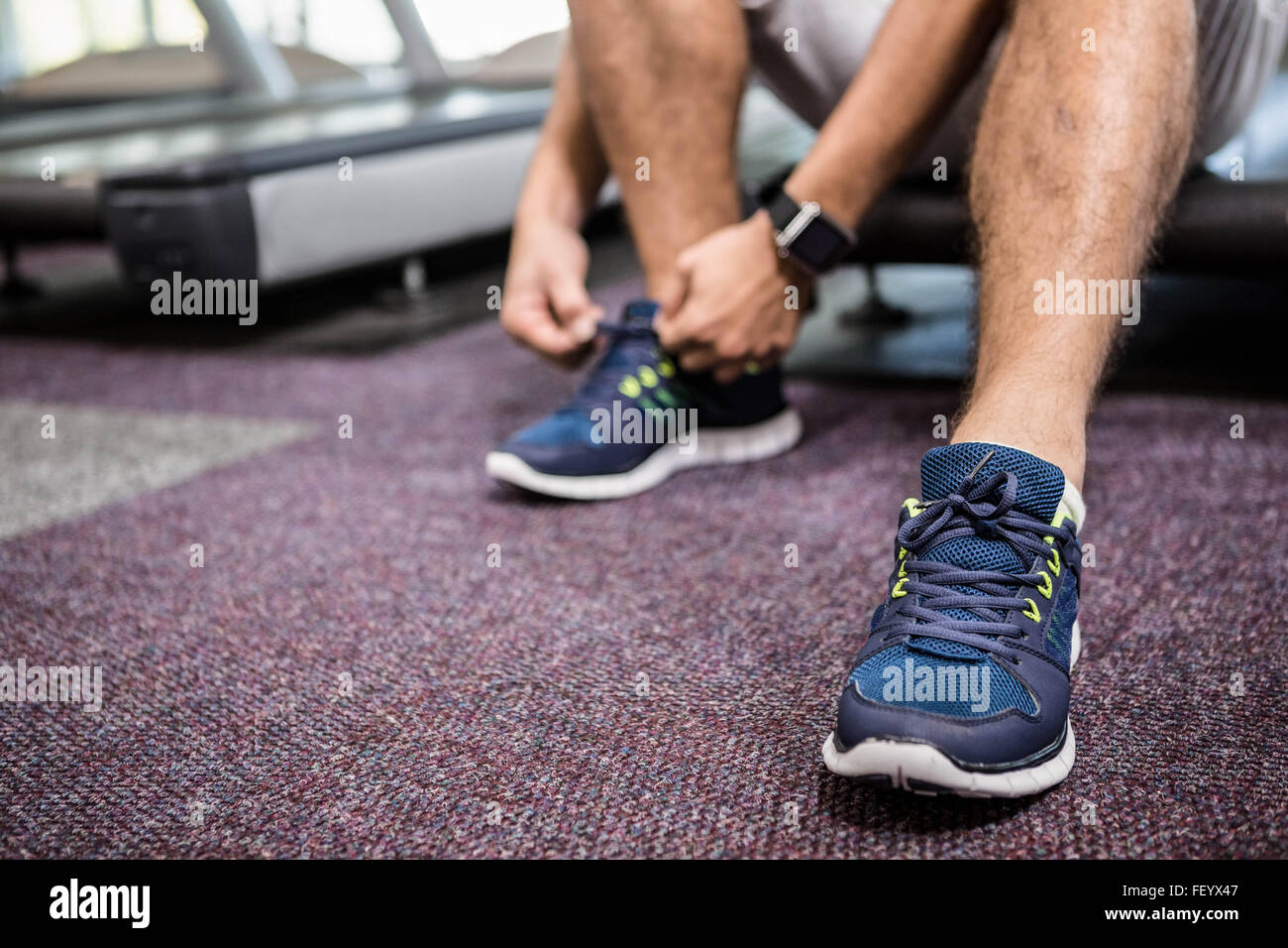 Lower section of man sitting on treadmill and tying the shoelace Stock Photo