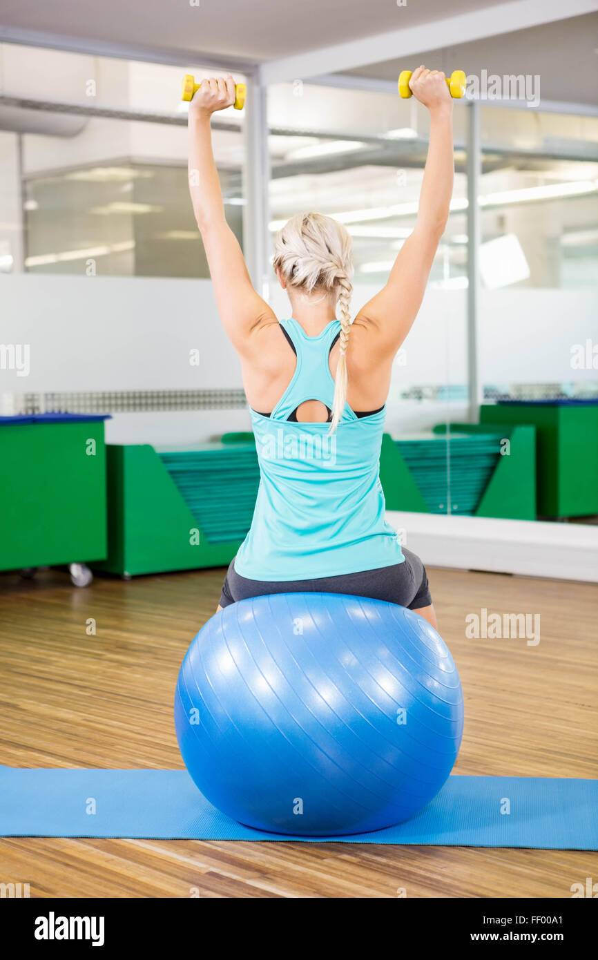Fit woman lifting dumbbells and sitting on exercise ball Stock Photo