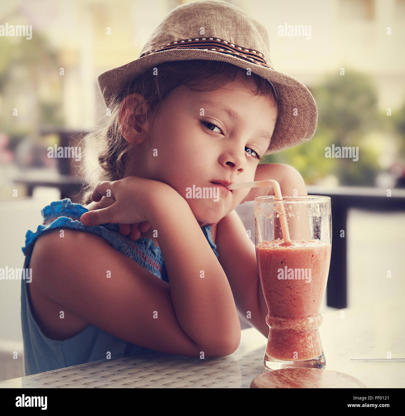 Clever serious kid girl drinking vitamin smoothie juice in street cafe ...