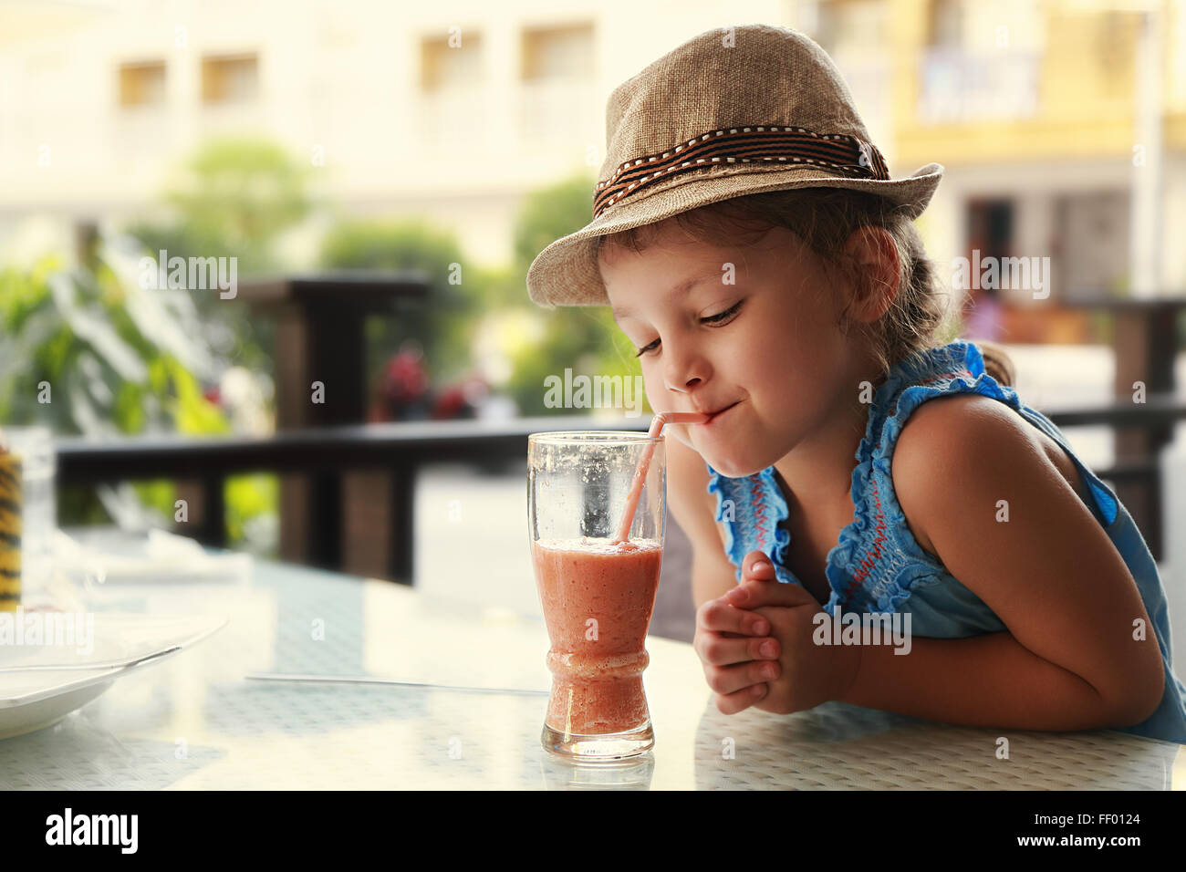 Cute thinking kid girl drinking tasty juice in street restaurant Stock Photo
