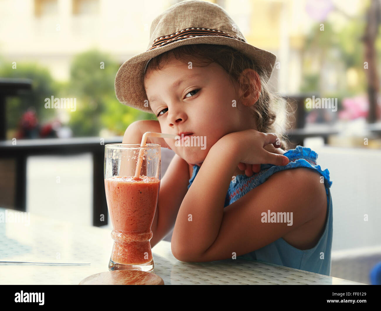 Clever serious kid girl drinking vitamin smoothie juice in street cafe ...