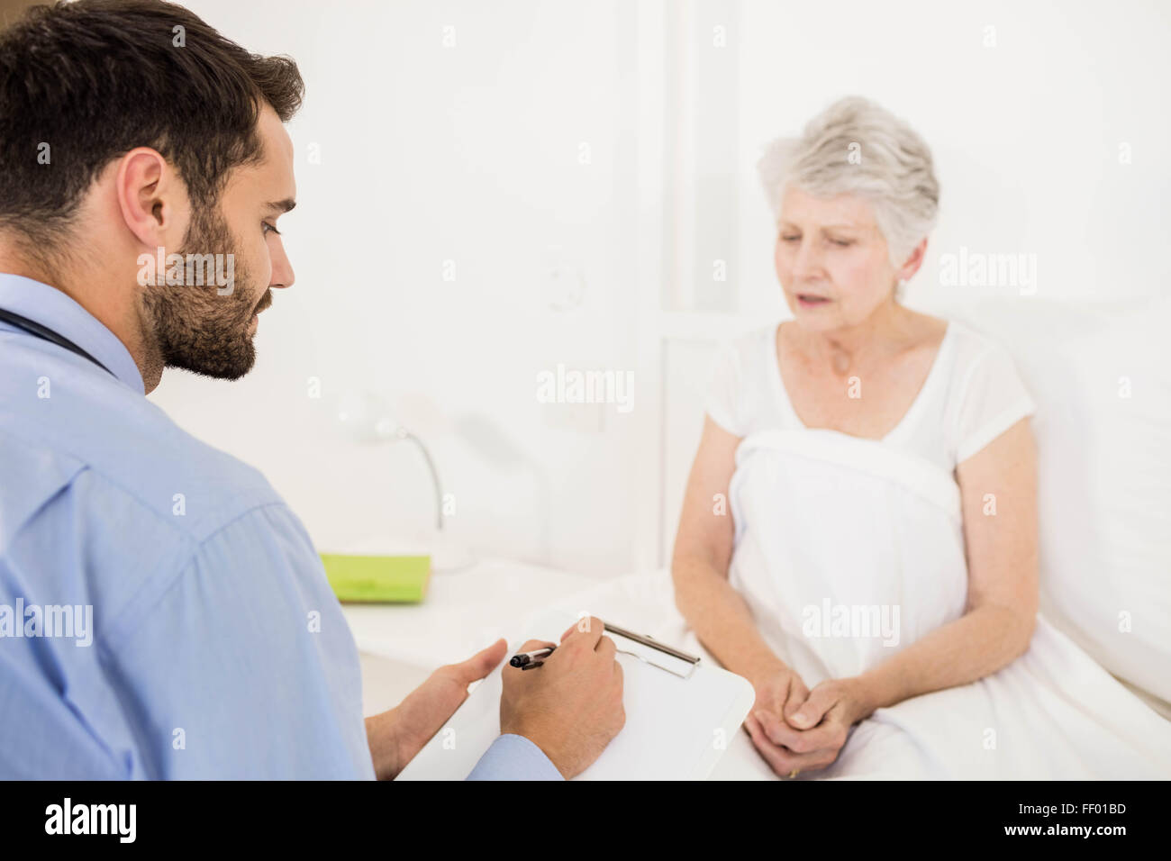 Home nurse listening to elderly woman and writing on clipboard Stock Photo