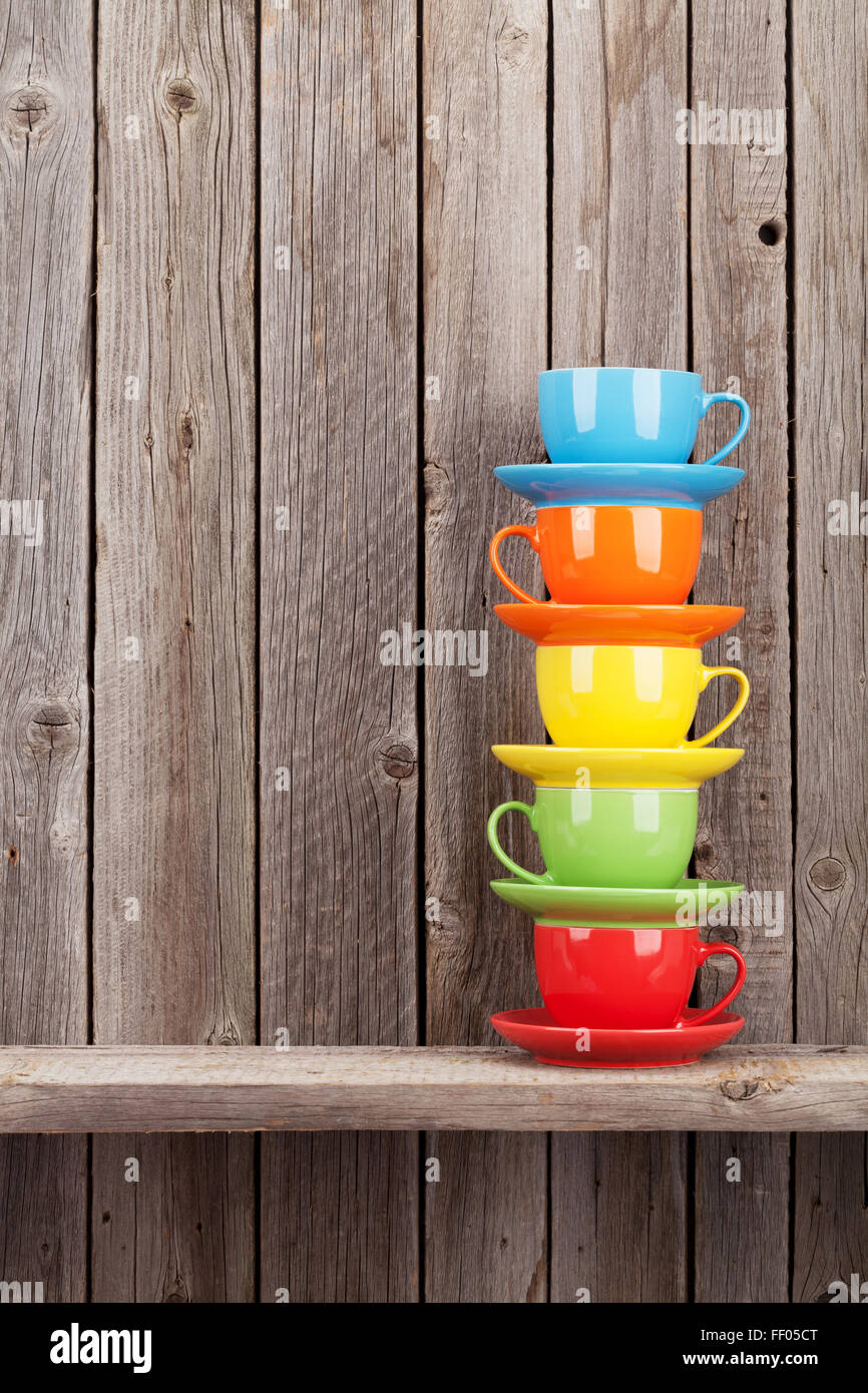 Colorful coffee cups on shelf against rustic wooden wall with copy space Stock Photo