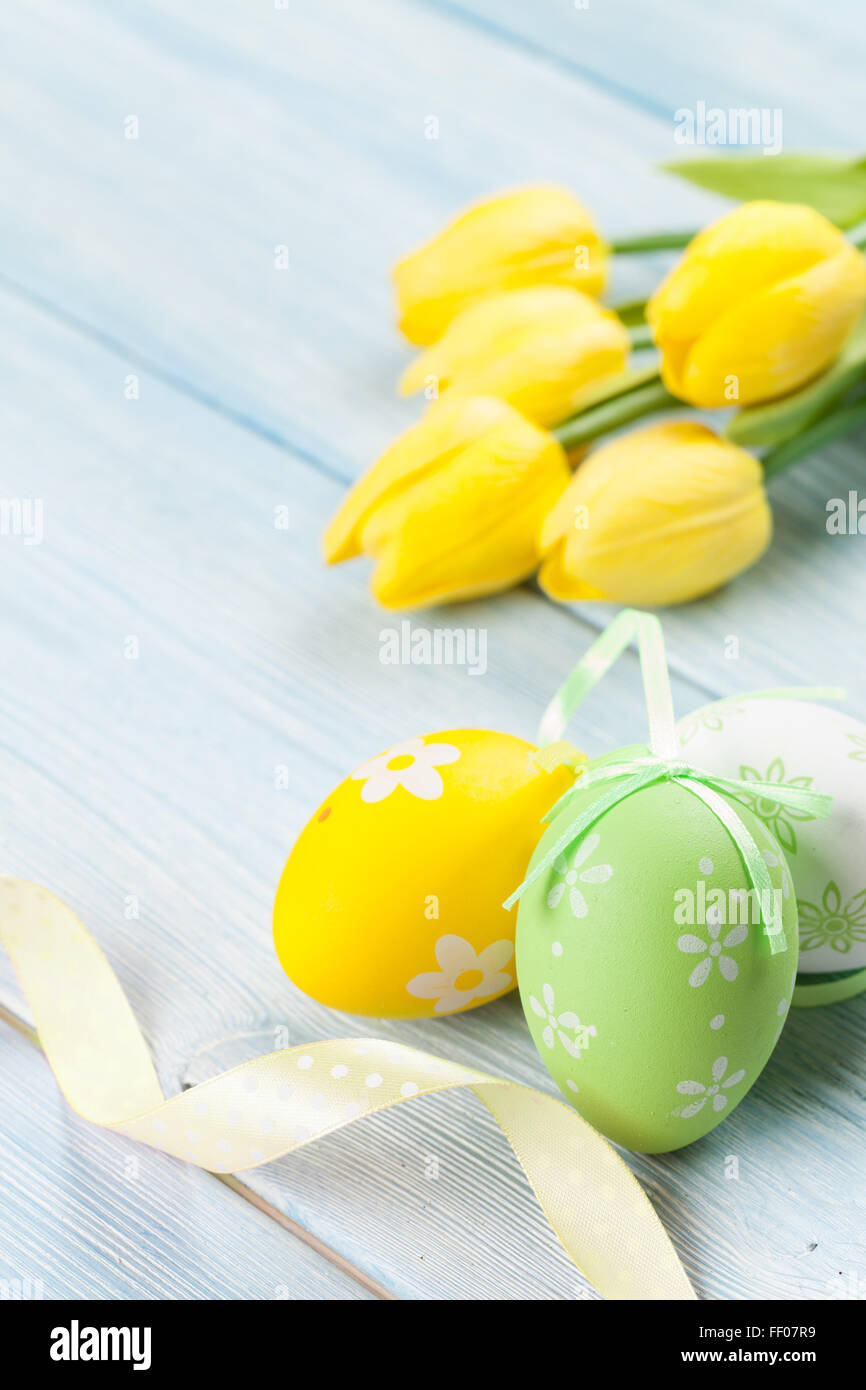 Easter eggs and yellow tulips over wooden background with copy space ...