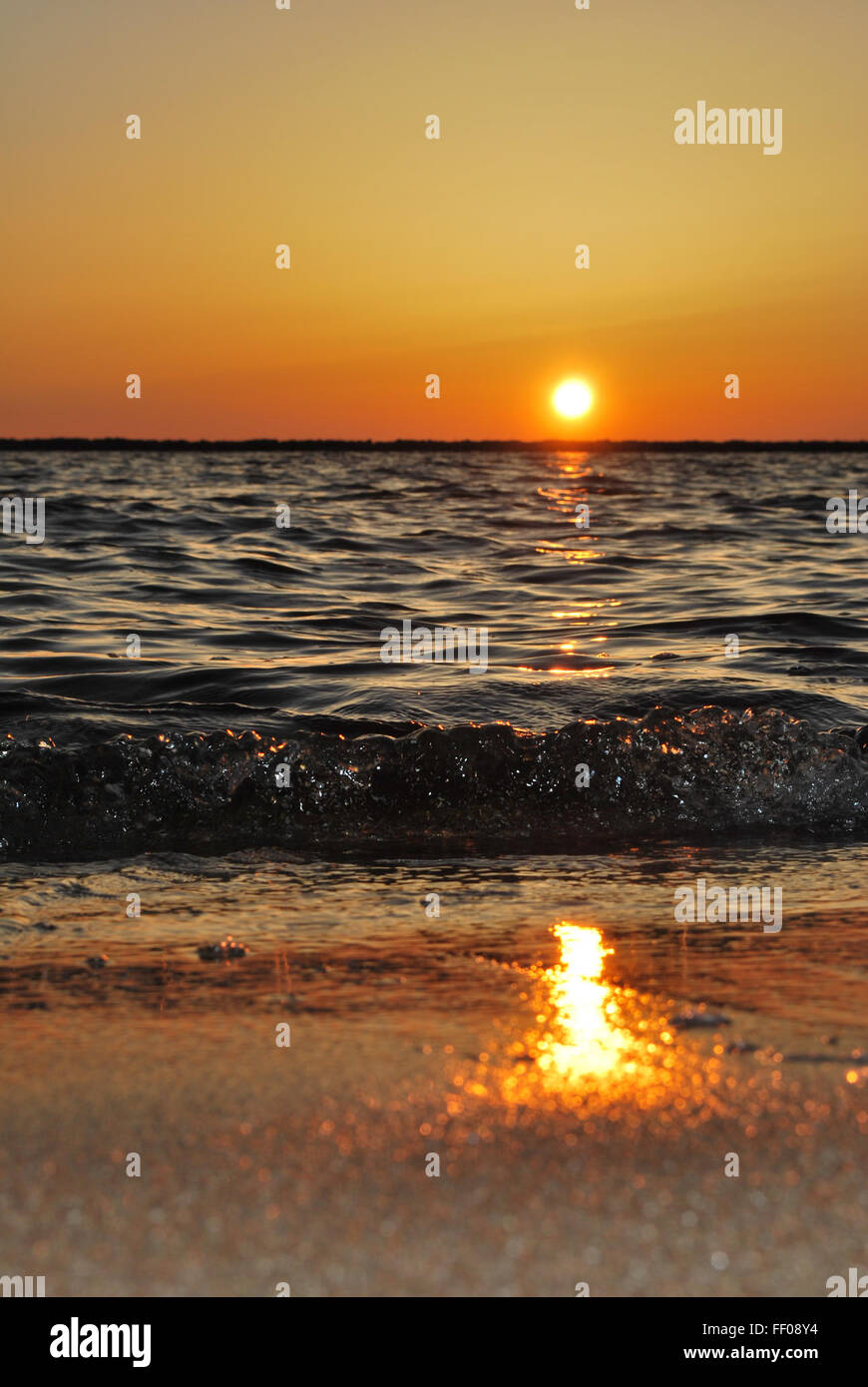 Ocean waves crashing on the shore at sunset, with the sun’s reflection ...