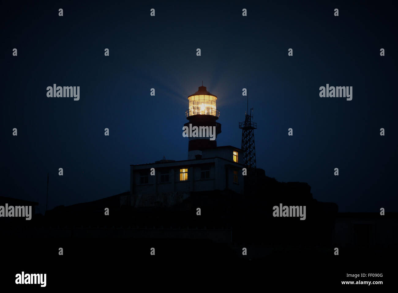 A lit lighthouse standing tall against the dark, night sky. The beacon ...