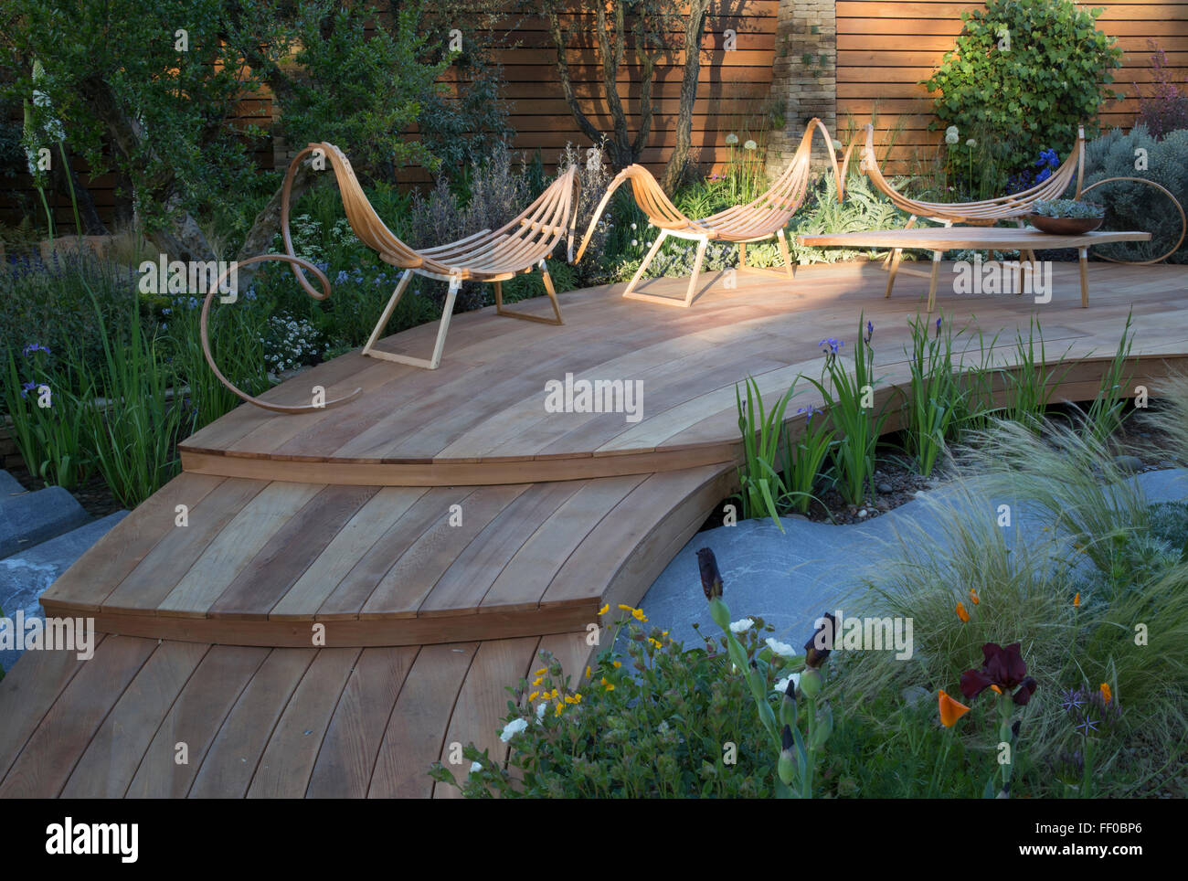 small modern spring show garden with wooden patio decking deck garden furniture seating area over water feature pond at Chelsea flower show london UK Stock Photo