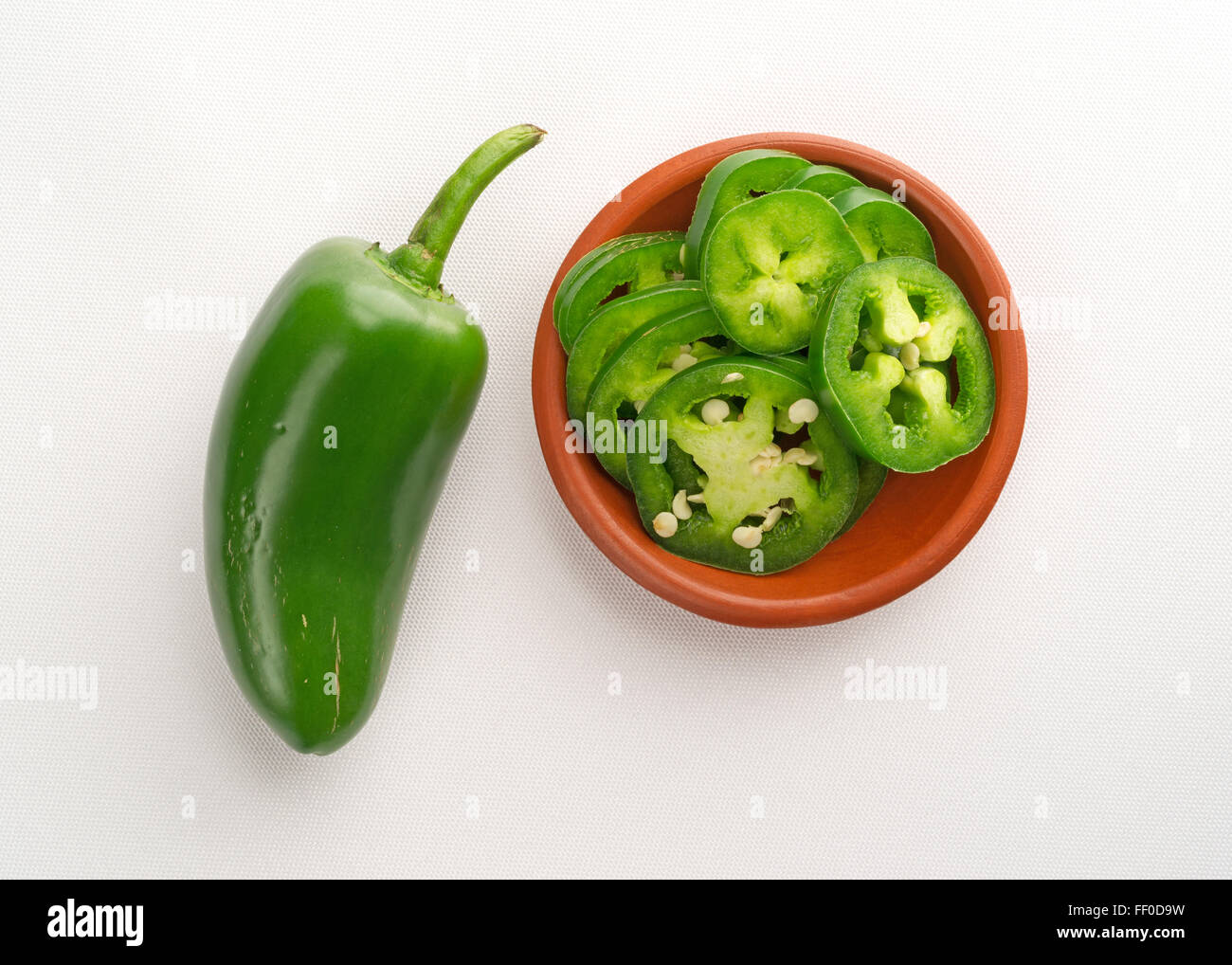 Top View Of A Small Bowl Of Sliced Jalapeño Peppers Plus A Large Whole