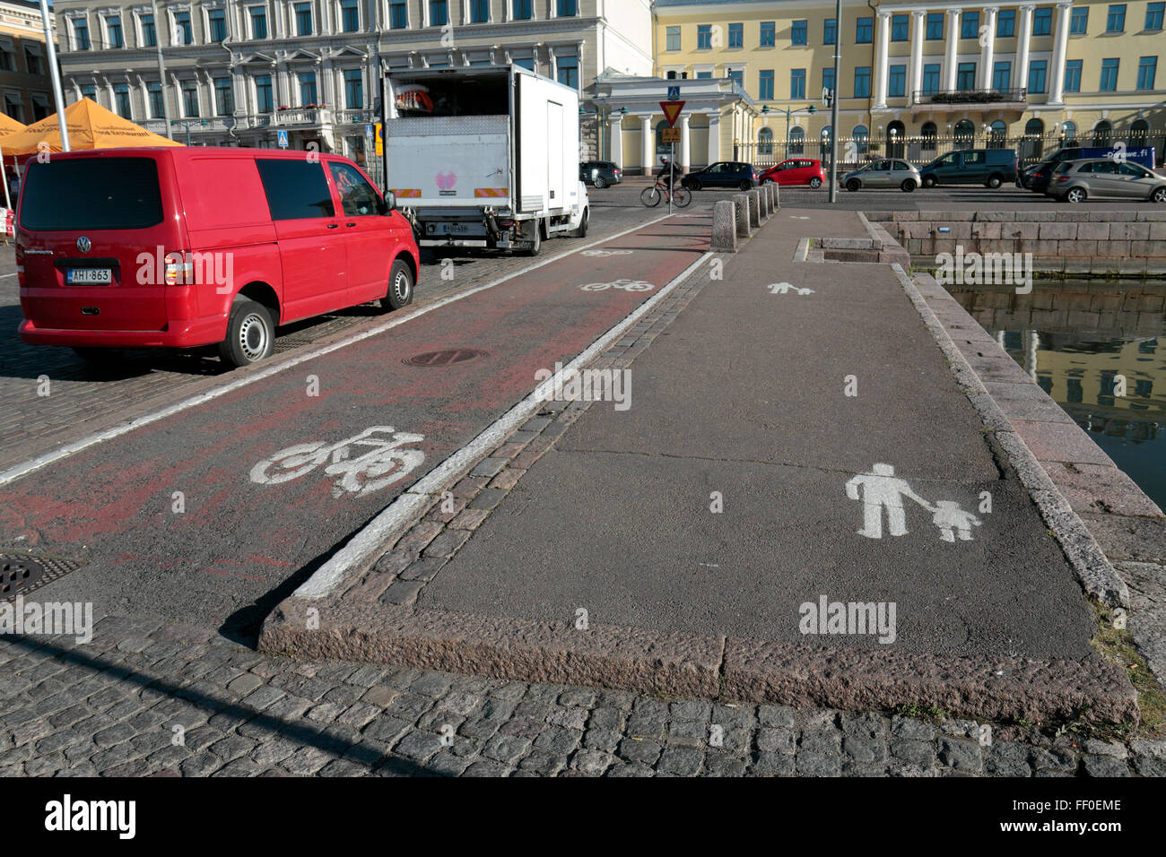 A wide pedestrian pavement beside a wide cycle lane beside a line of traffic in Helsinki, Finland. Stock Photo
