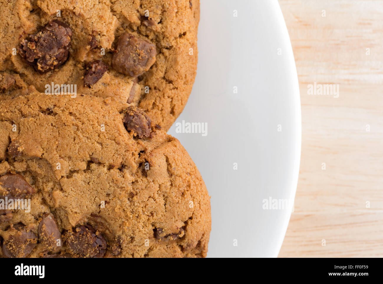 Top close view of a plate of milk chocolate chip cookies on a wood table illuminated with natural light. Stock Photo