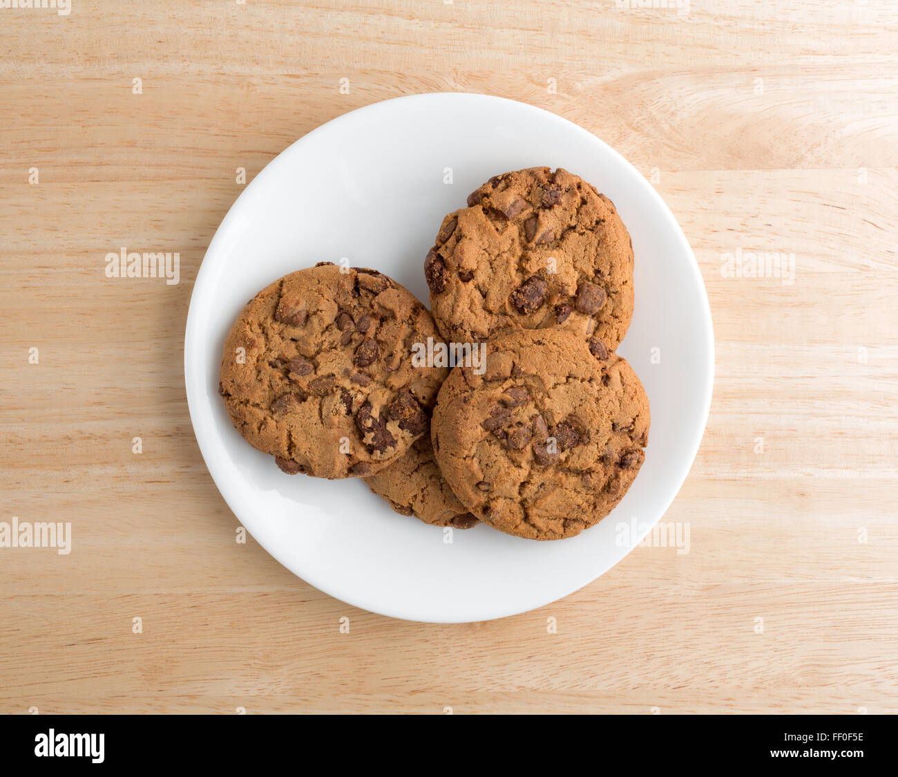 Top view of a plate of milk chocolate chip cookies on a wood table illuminated with natural light. Stock Photo