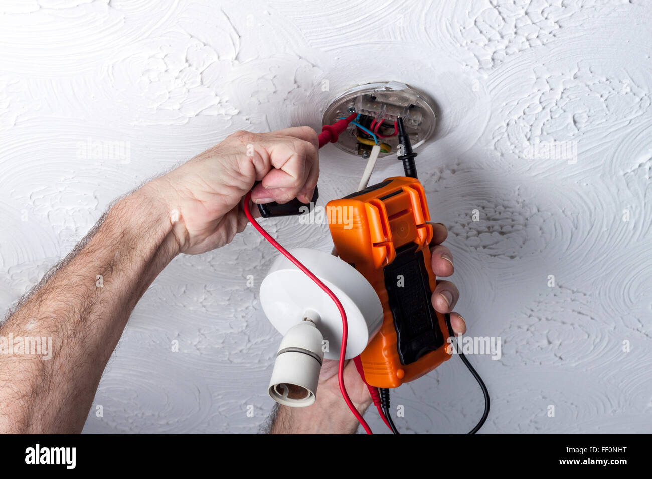 Electrician testing a ceiling mounted light fitting with a multimeter
