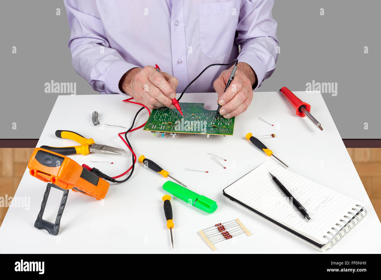 Electronic test engineer using a multimeter to test a curcuit board on his white topped work bench Stock Photo