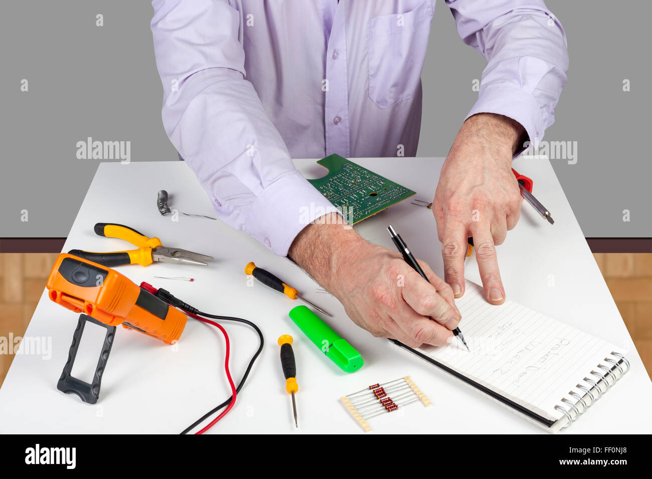 Electronic test engineer writing his circuit testing results in a note pad on his white topped