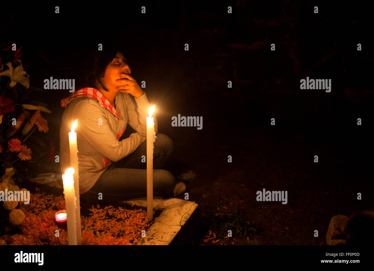 A girl sits in a tomb decorated with candles and yellow marigold