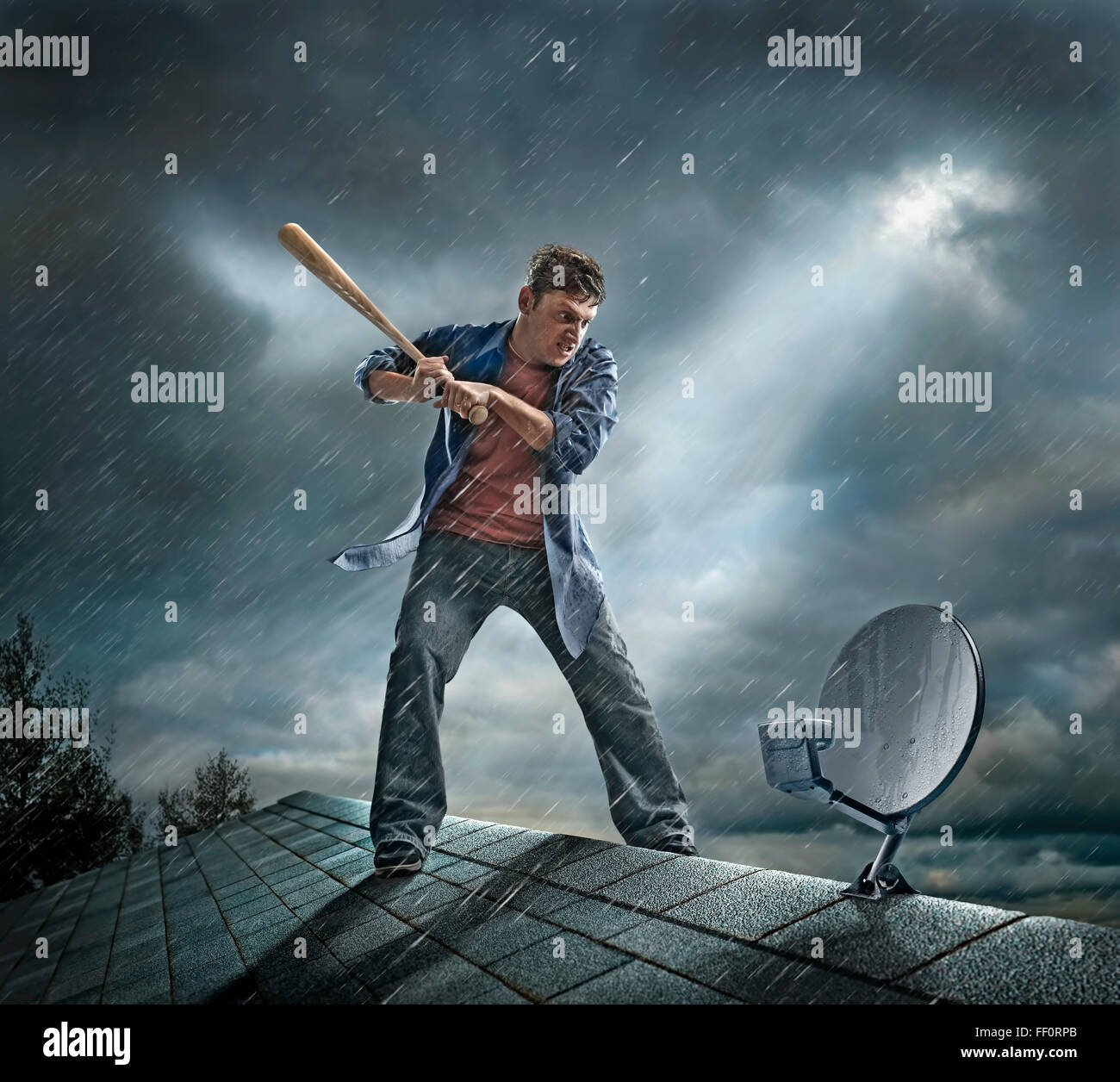 Caucasian man swinging baseball bat at satellite dish on roof Stock Photo