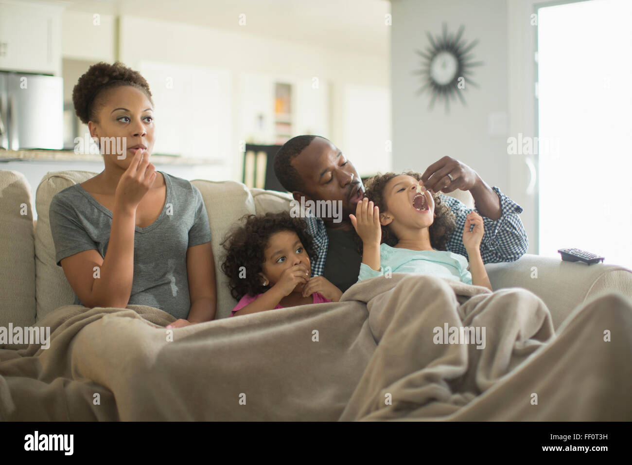 Family in blanket snacking on sofa Stock Photo