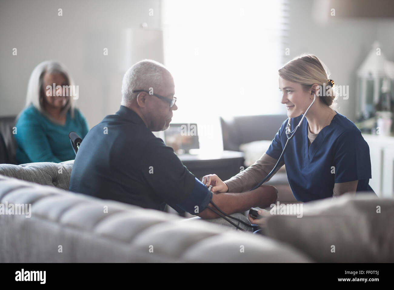 Nurse taking patient blood pressure in living room Stock Photo