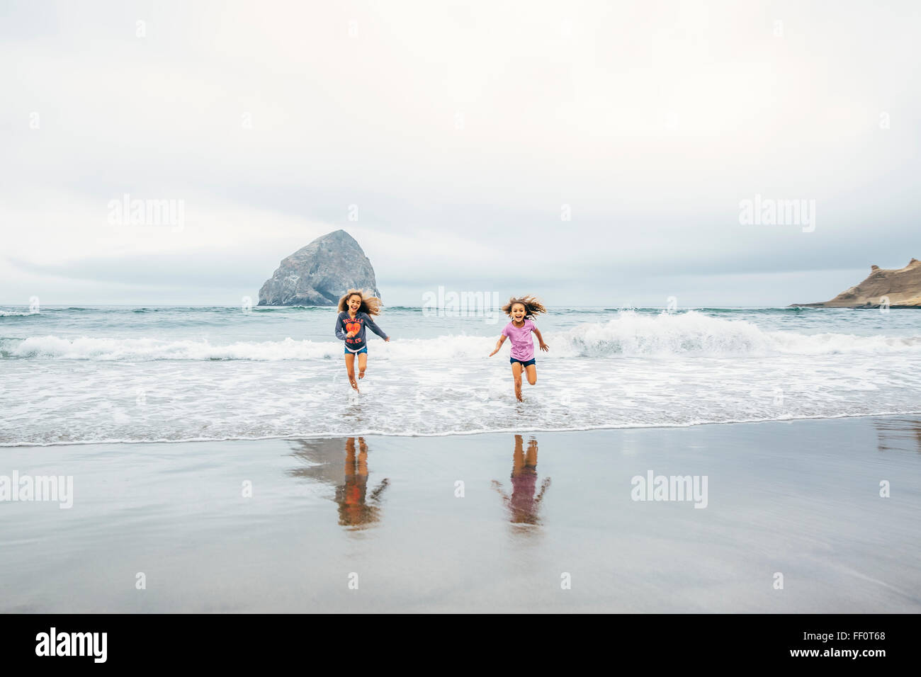 Mixed race sisters running on beach Stock Photo