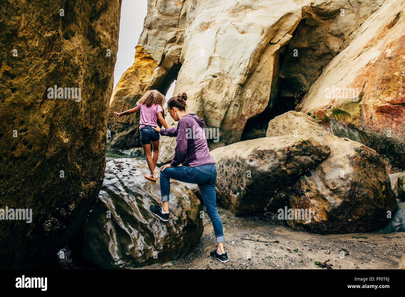 Mother and daughter climbing on beach rocks Stock Photo