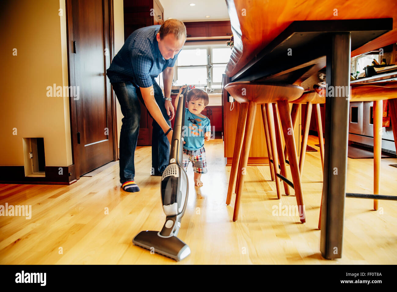 Father and son vacuuming kitchen Stock Photo