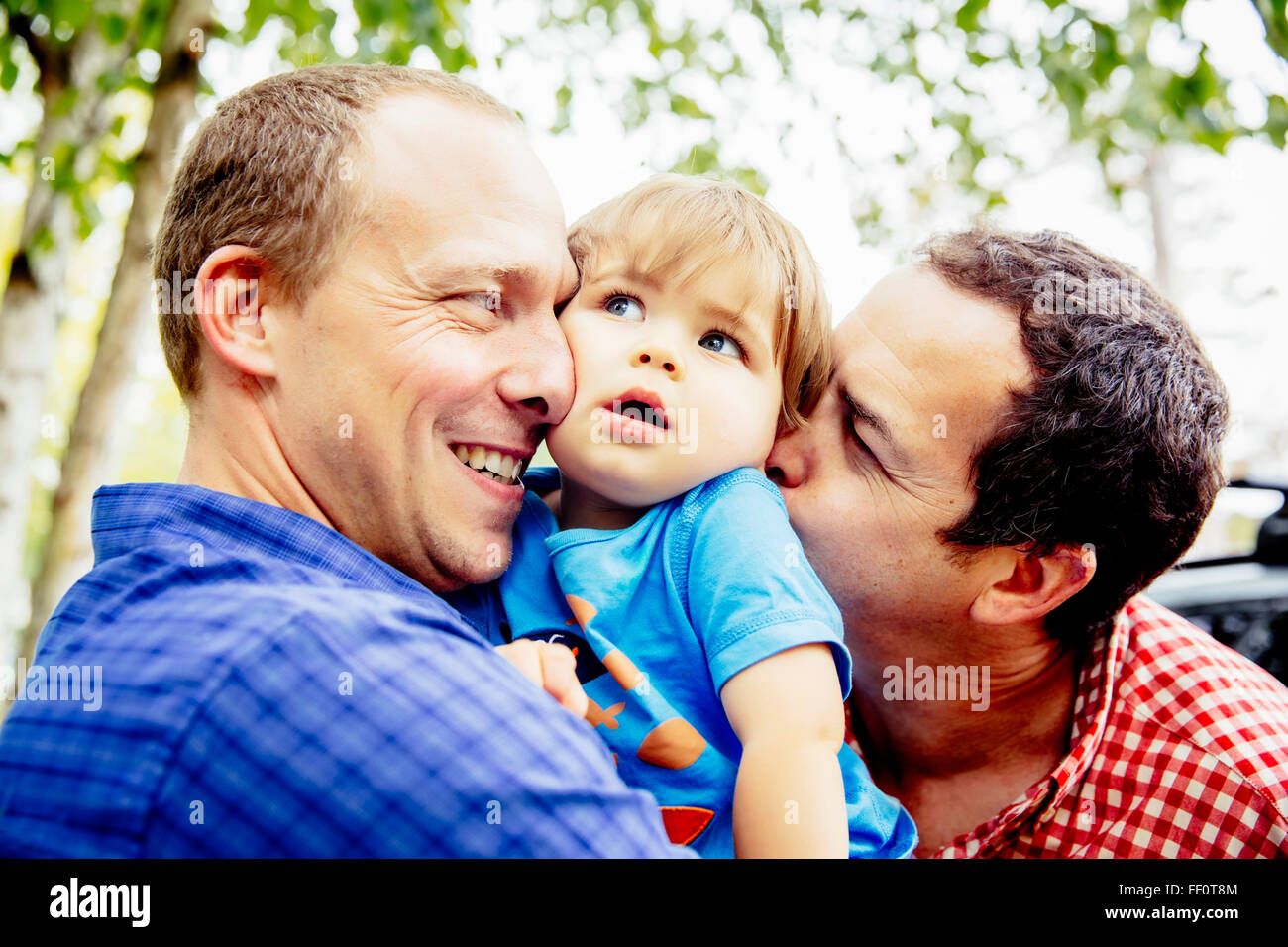 Gay fathers kissing baby son outdoors Stock Photo