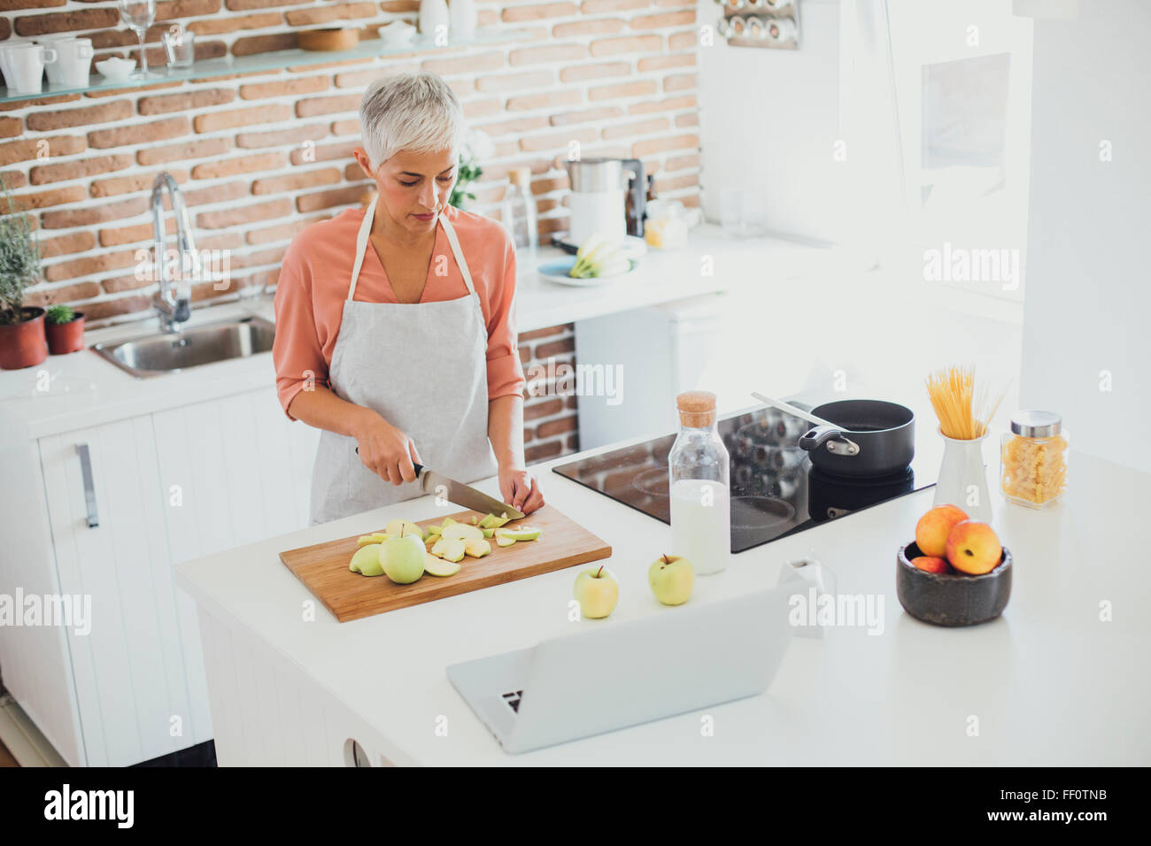 Older Caucasian woman cutting apples in kitchen Stock Photo