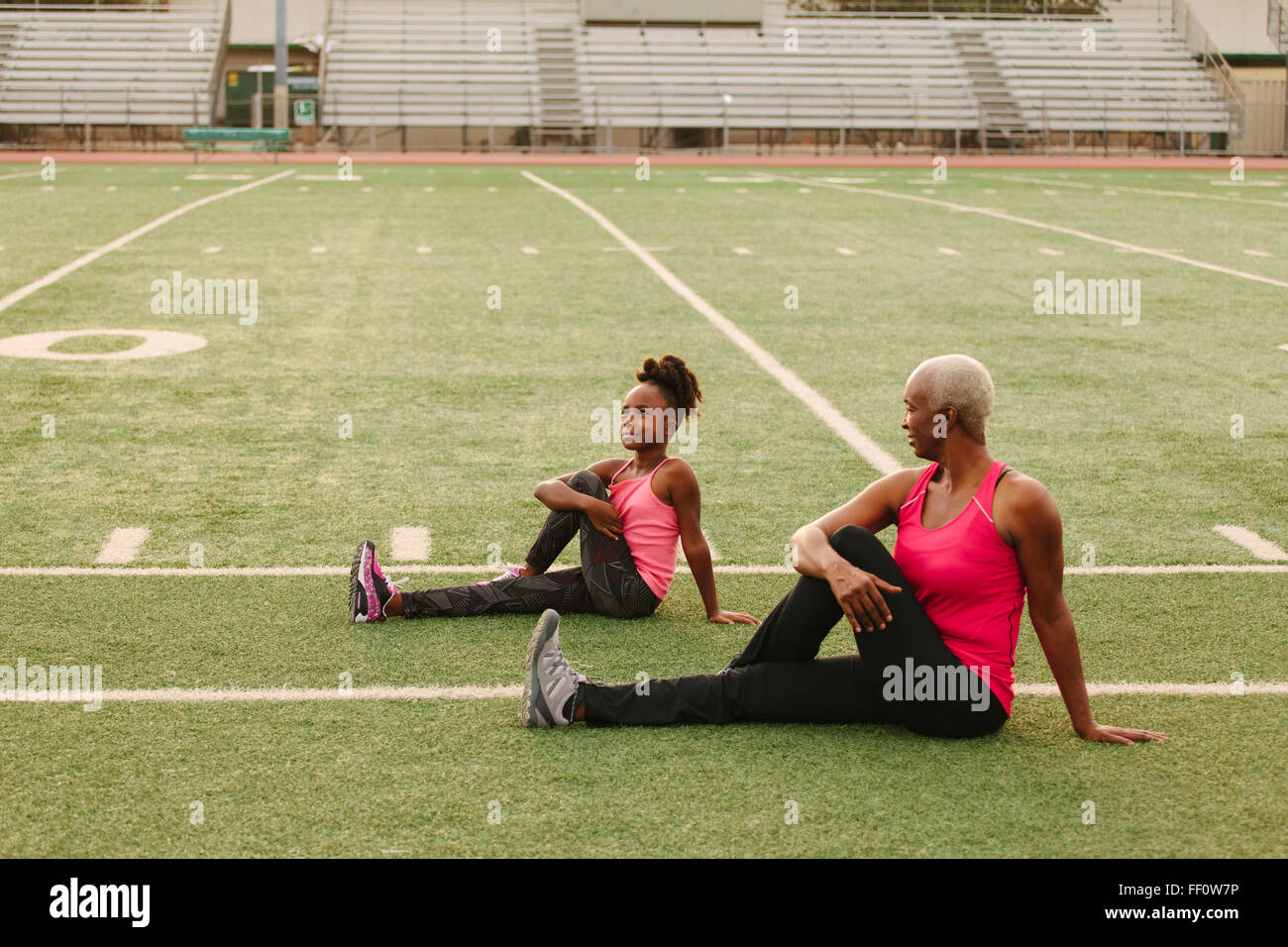 Grandmother and granddaughter stretching on football field Stock Photo