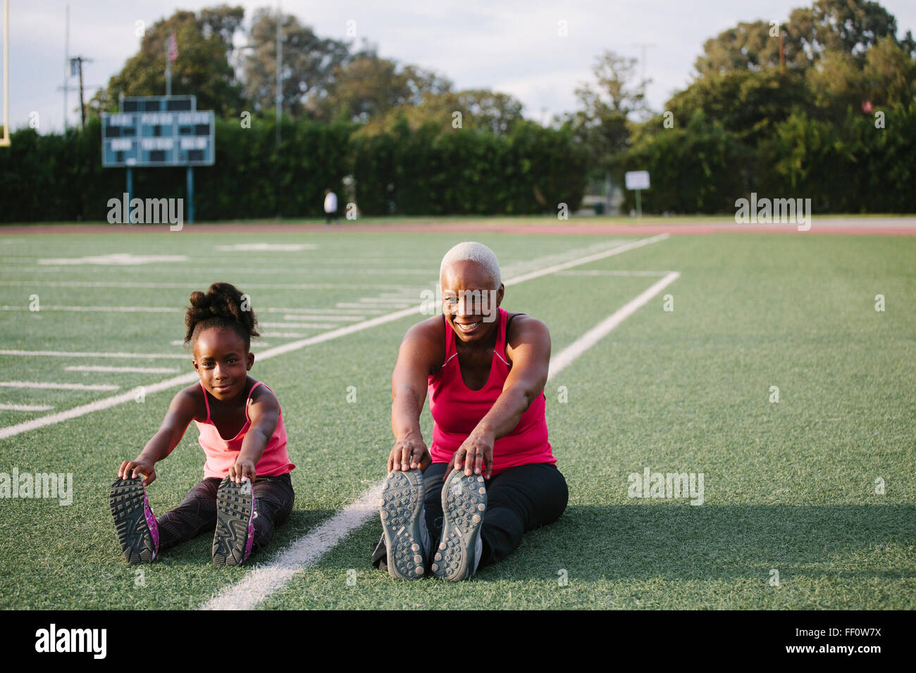 Grandmother and granddaughter stretching on football field Stock Photo