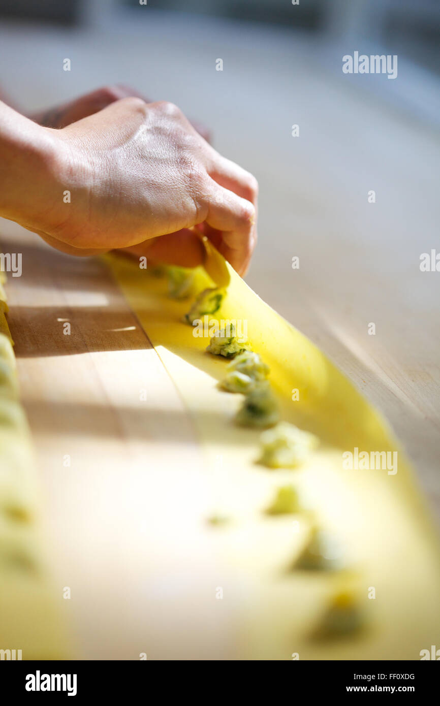 View of A close-up on hands folding homemade pasta dough over small dots of ...