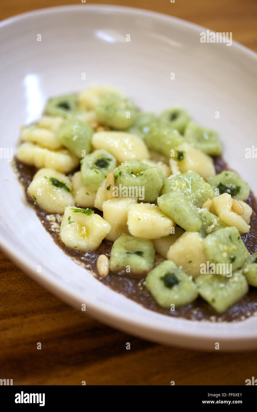 A prepared dish of gnocchi on top of sauce and sprinkled with dots of pesto and pine nuts. Stock Photo