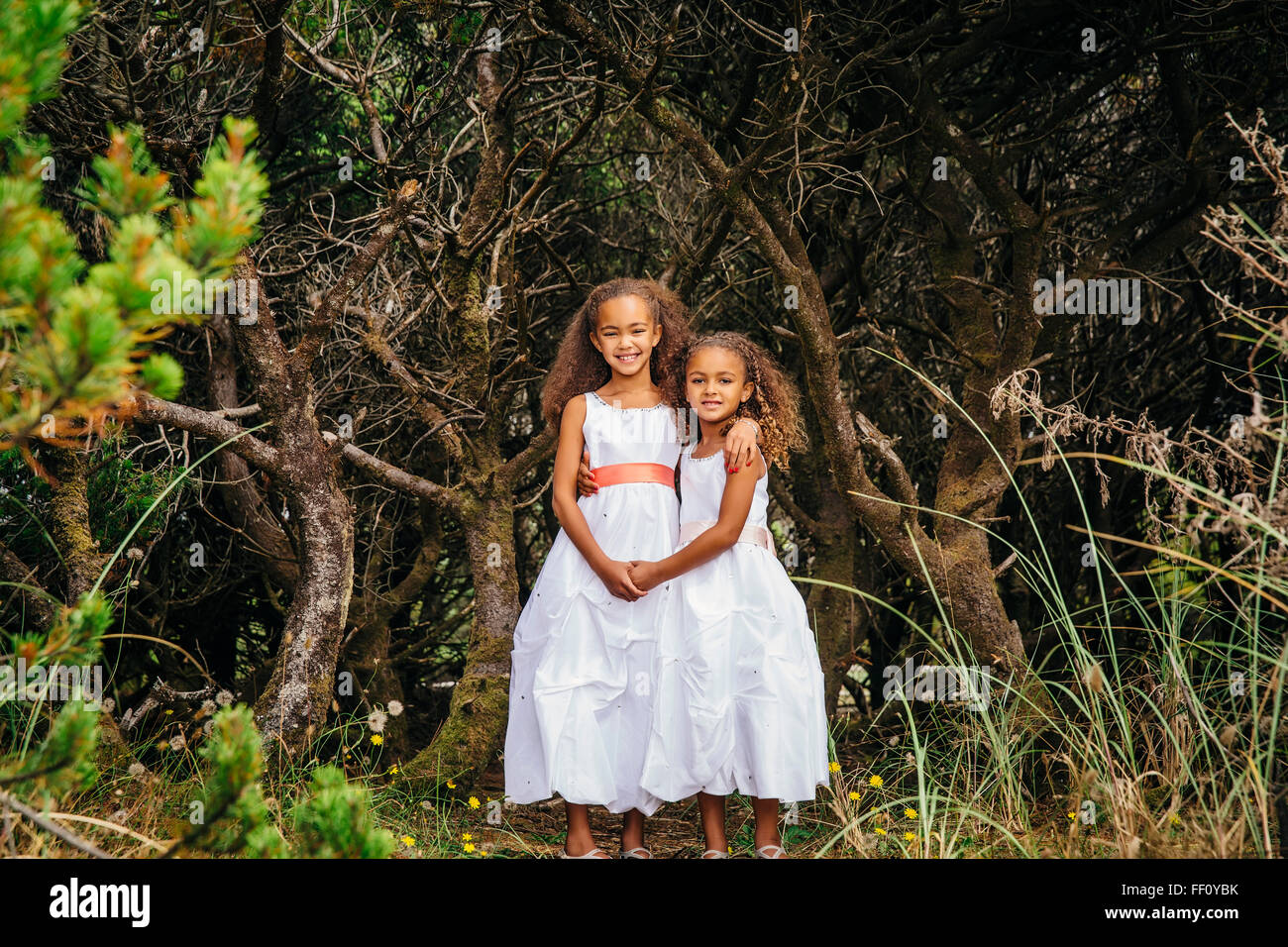 Mixed race sisters wearing dresses in garden Stock Photo