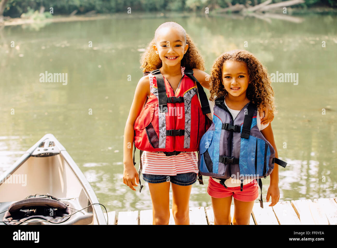 Mixed race sisters wearing life jackets at lake Stock Photo
