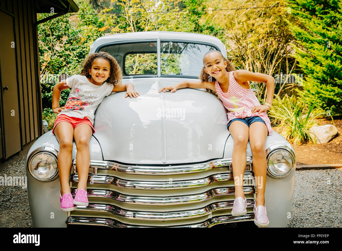 Mixed race sisters sitting on vintage car Stock Photo