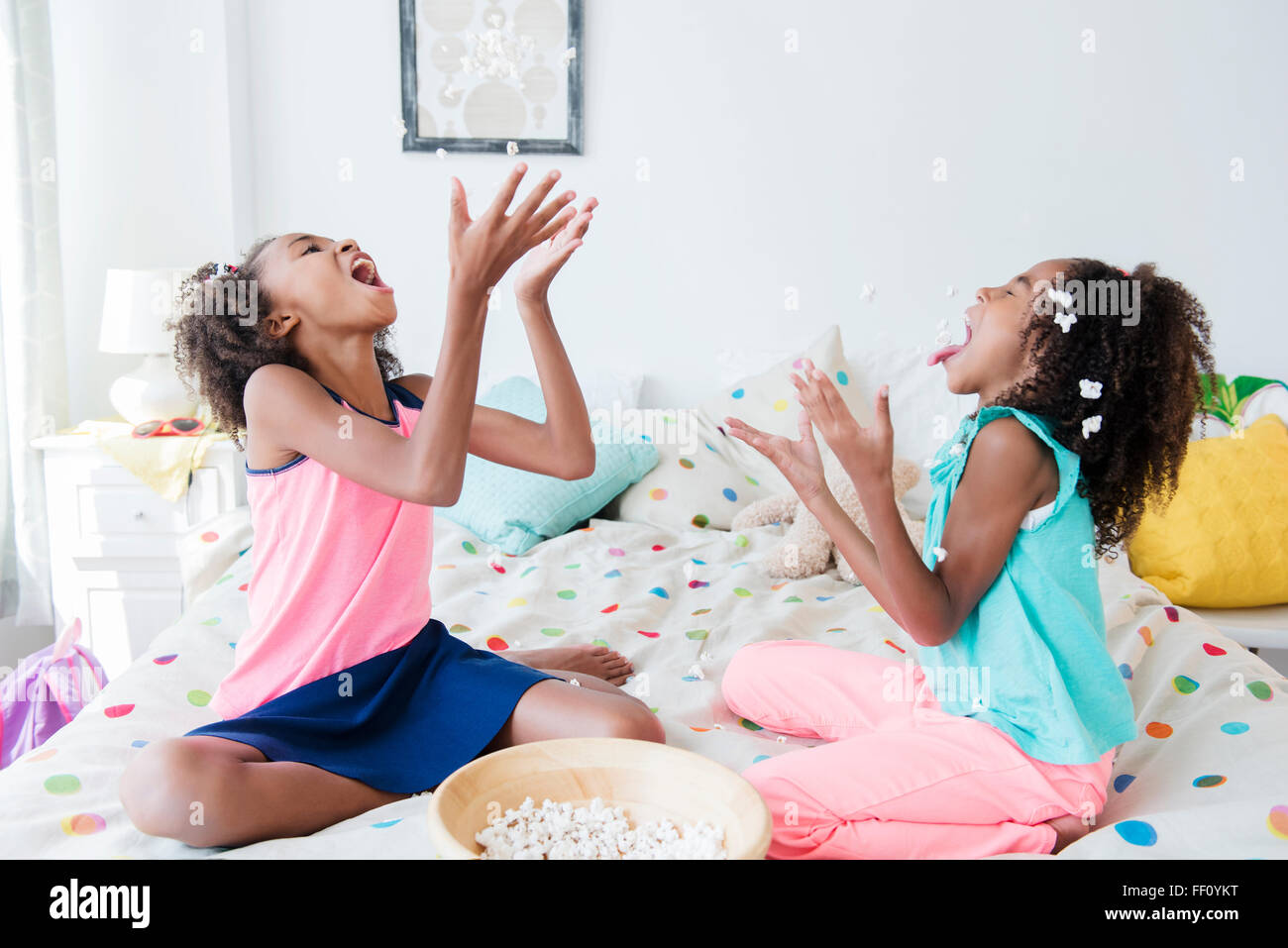 Mixed race sisters eating popcorn on bed Stock Photo