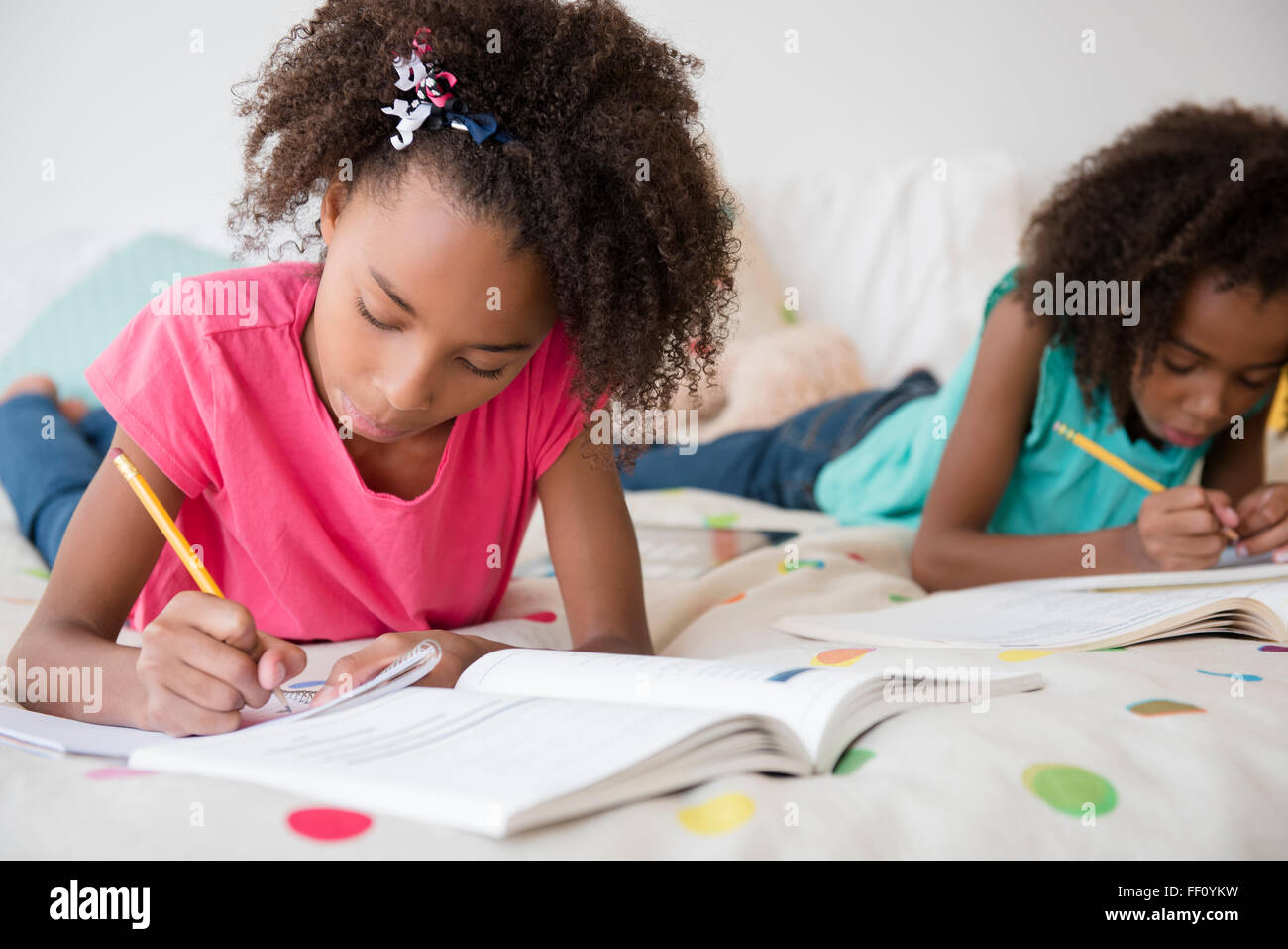 Mixed race sisters doing homework on bed Stock Photo