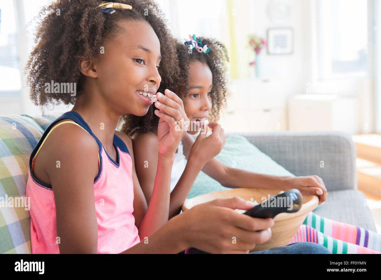 Mixed race sisters watching television on sofa Stock Photo