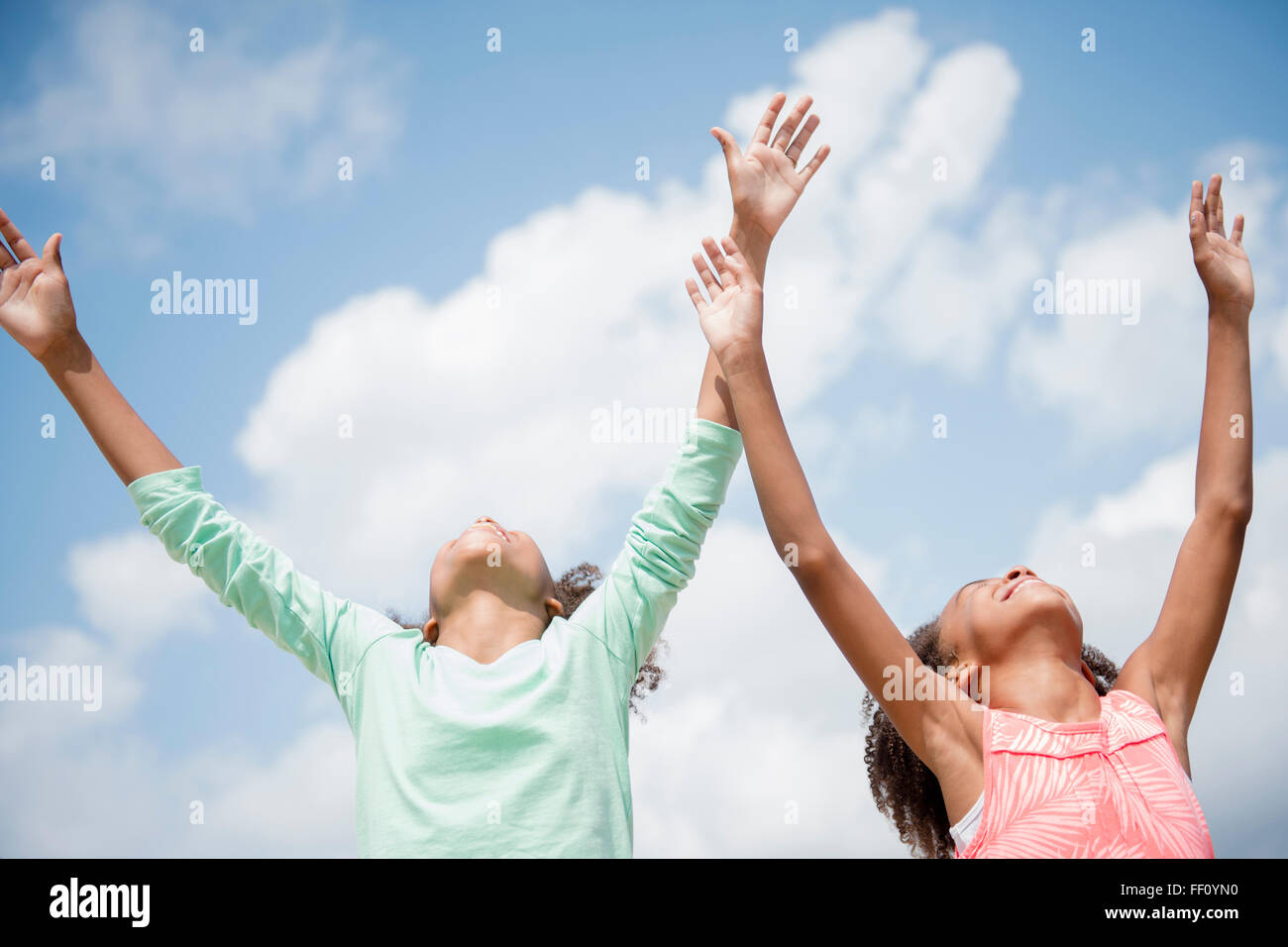 Mixed race sisters cheering in blue sky Stock Photo